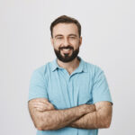Home portrait of a handsome bearded man smiling looking to the camera with his hands crossed isolated on white background. this person looks like an ordinary guy who is sincere and ready to help everyone.